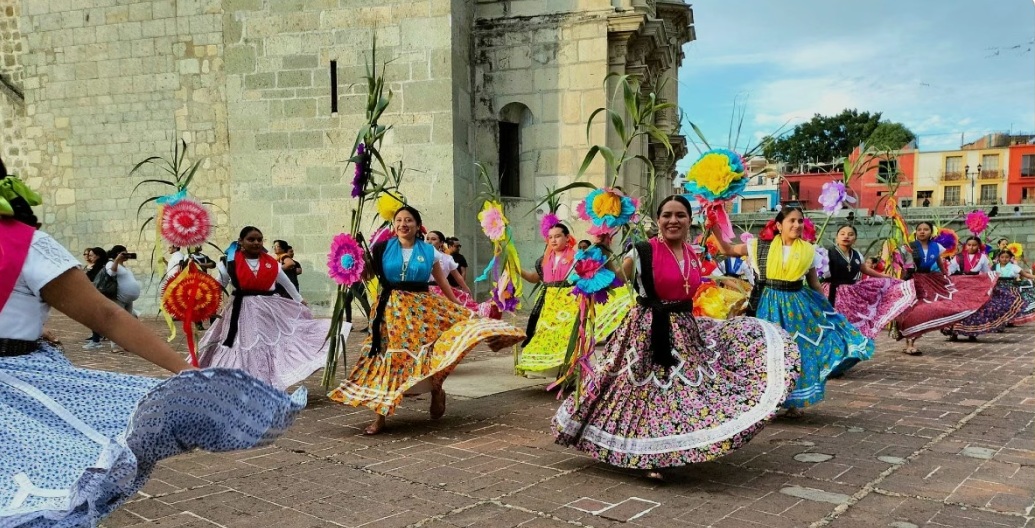 Mujeres con trajes tradicionales bailando frente a una iglesia en Oaxaca